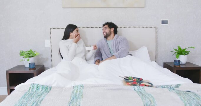 African American couple on bed holding positive test stick, reacting, smiling with breakfast tray