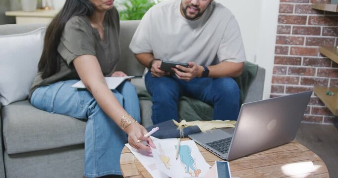 Couple sitting on sofa, woman picking character sheet, man using tablet, both annotating designs