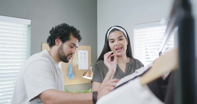 African American couple selecting outfits in studio as man pointing at rack, woman checking hangers