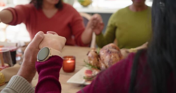 Family joining hands bowing in thanks, then passing bread basket and serving turkey at dining table
