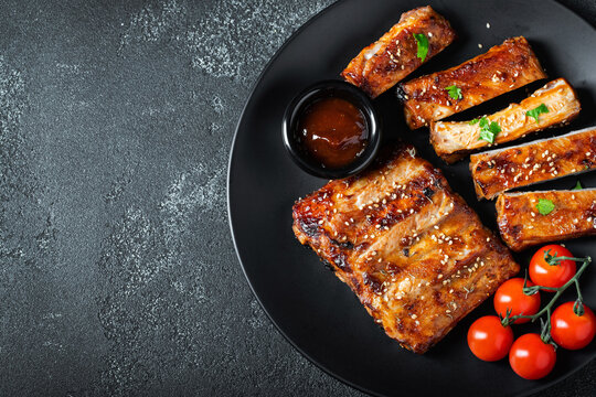 Hot grilled spare ribs from a summer BBQ served on a plate with sauce. Top view. Copy space