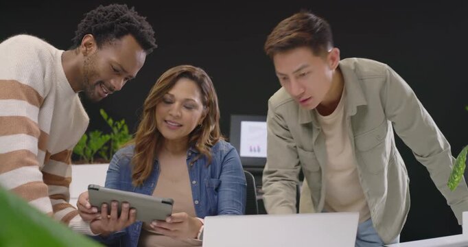 Diverse coworkers reviewing tablet showing draft and using laptop at office, approving launch