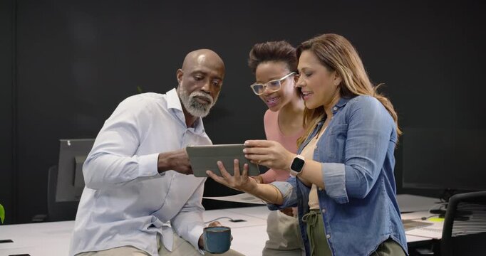 Coworkers gathering at office around tablet, woman presenting it, man tapping tablet, reviewing