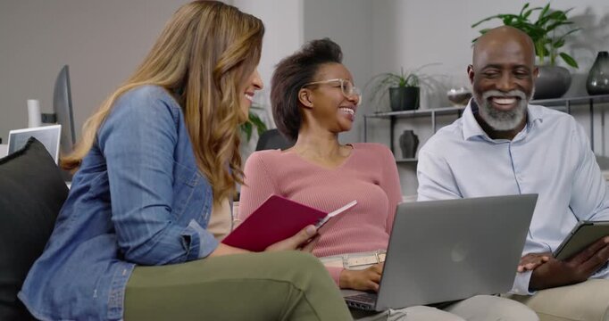 African American team meeting in lounge left holding notes, center typing laptop man tapping tablet