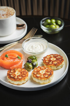 Savory Syrniki with Smoked Salmon, Olives and Sour Cream on White Plate