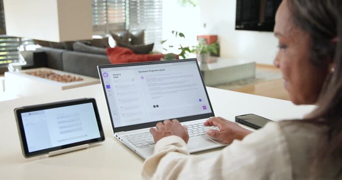 African American woman editing proposal on laptop, replying to tablet chat at counter, copy space