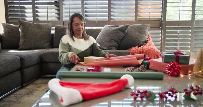 African American woman in green sweater picking up orange paper in living-room, wrapping gifts