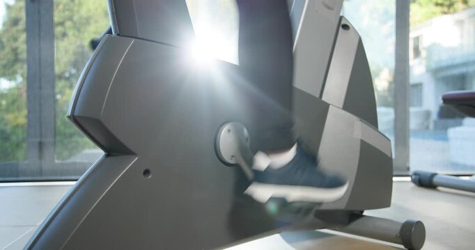 Sun flare through window is starting action as person's lower leg is pedaling bike for cardio