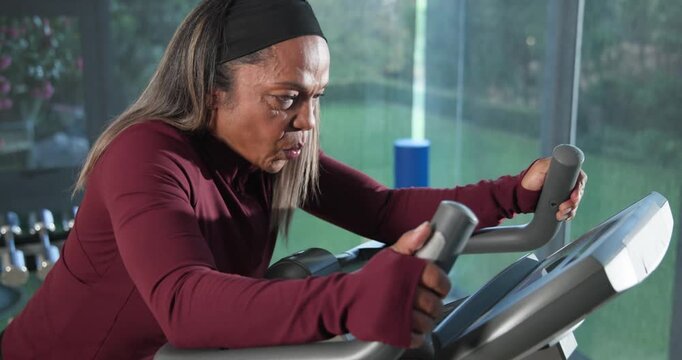 Mature African American woman starting on elliptical at home gripping console, maroon top training