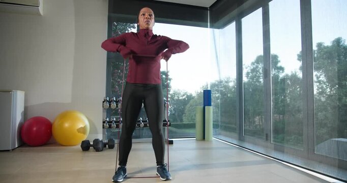 African-American woman in maroon top doing upright rows at home with band under feet for strength