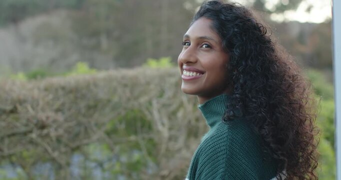 African woman beside hedge in green knit, soft daylight drawing smile and lifting gaze, copy space