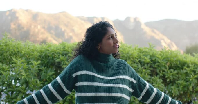 African American woman standing on deck in sweater, turning chin up, sun drawing gaze toward range