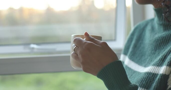 Man is placing white mug near window, adjusting grip and rotating cup to warm hands