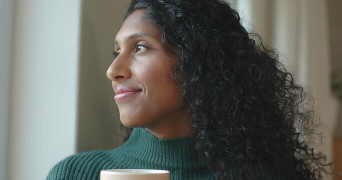 African American woman in green top sitting by window holding pale mug light drawing gaze thinking