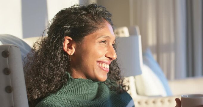 African American woman in green top sitting in armchair holding mug, sunlight lighting face smiling