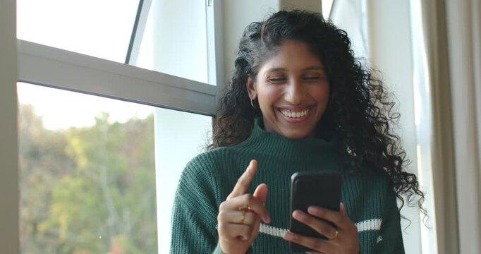 African American woman at window in green sweater reading message, tapping phone, gold ring showing