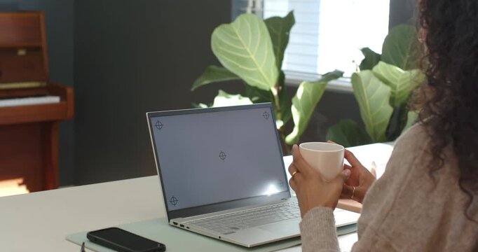 Woman is entering frame holding mug at desk, moving closer to laptop and preparing to sip