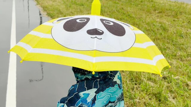A cute panda umbrella shields a person walking along a wet path. The bright scene feels cheerful, cozy, and playful against the rainy backdrop.