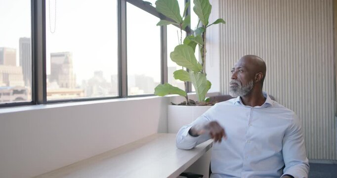 Mature African man sitting at desk by window camera pushing adjusting collar smiling, copy space