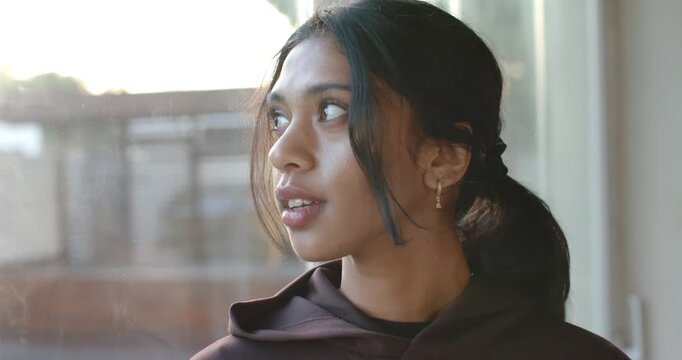 Indian woman standing at window, sunlight drawing gaze, turning, smiling, meeting camera