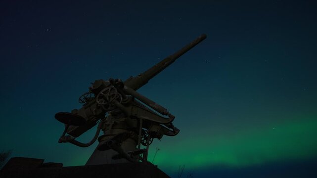 View of a historic anti-aircraft gun at Suomenlinna fortress under the vibrant green glow of the aurora borealis in the night sky in Helsinki, Uusimaa, Finland. Timelapse.