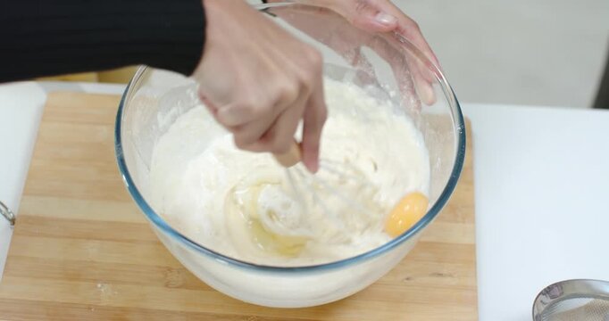 Whisk is beating and folding batter in bowl at kitchen counter to incorporate added eggs