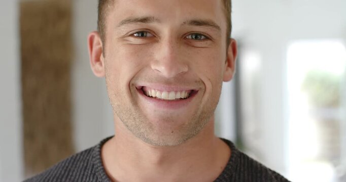 Man in mid 20s holding gaze, shifting into smile preparing portrait in hall wearing ribbed sweater