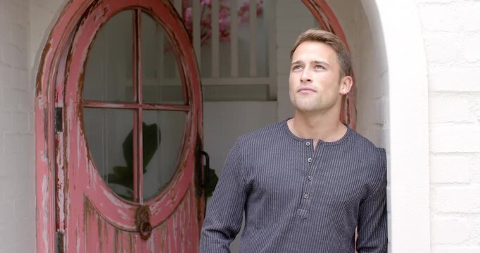 Man wearing henley leaning, straightening smiling at entry as framing shift by pink door
