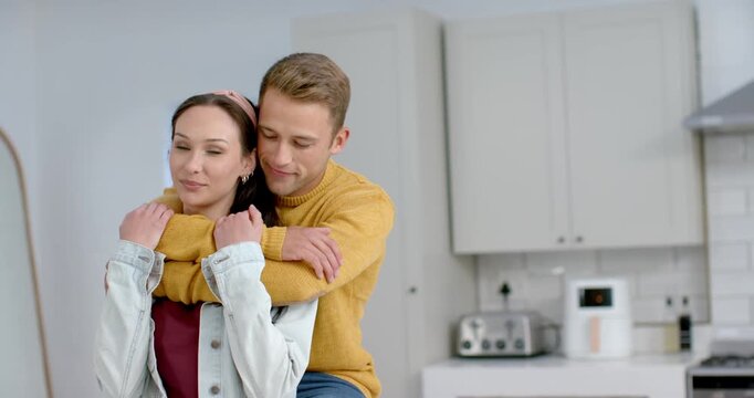 Couple hugging near toaster in kitchen with man approaching from behind, wrapping arms, whispering