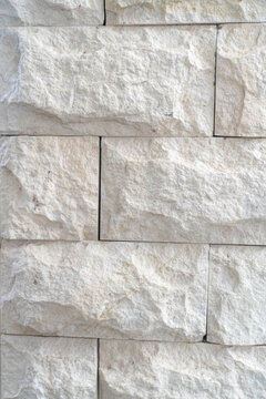Close up view of a white, split face natural stone wall cladding, composed of rectangular blocks featuring a rough, chiseled texture. 