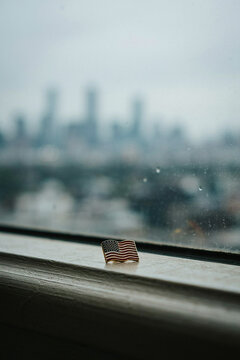 911, small american flag pin on a windowsill with blurry rainy city skyline view