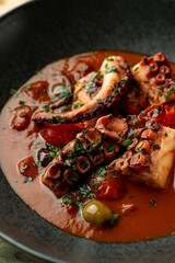 Delicious octopus stew simmering with vibrant tomatoes and herbs in a black bowl © Tkachenko Alexey