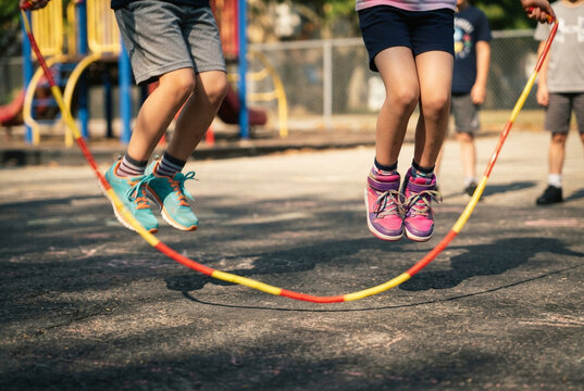 Children jumping over a long jump rope in a park setting.