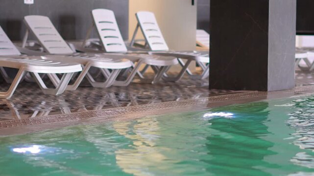 Indoor swimming pool with turquoise water and sun loungers lining the edge.

