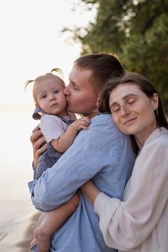 Loving parents embrace their baby daughter on a serene beach at sunset
