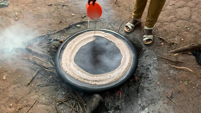 View of a person pouring batter onto a traditional circular mitad griddle over an open fire to cook injera bread in Ethiopia.