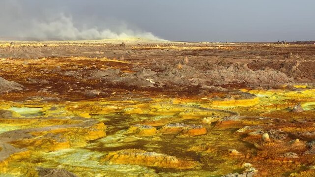 View of the colorful geothermal landscape of Dallol with mineral deposits and volcanic steam rising in the background in Ethiopia.