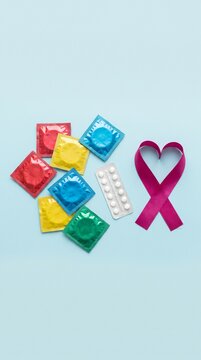 Vertical photo of colorful condoms and a pink awareness ribbon on a light blue background