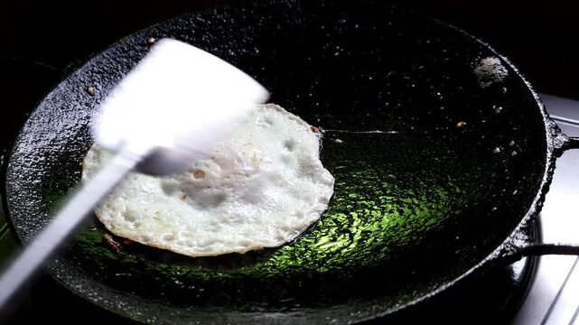 Lifting Sunny Side Up Fried Egg Sprinkled with Chili Flakes from Cast Iron Skillet - Cooking Breakfast and Culinary Concept