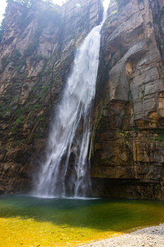 Majestic waterfall falling into an emerald pool beneath a rocky mountain cliff