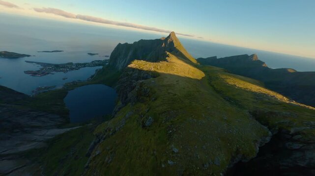 FPV aerial view of Lofoten mountains with a mountain lake and rocky terrain under a clear sky in Nordland, Norway.