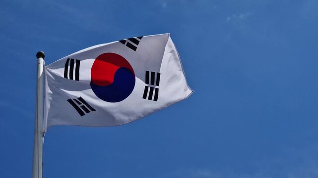 National flag of South Korea on a flagpole under a blue sky. Close-up of the national flag of the Republic of Korea fluttering in the wind against a clear blue sky. Concept of patriotism