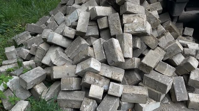 Stack of cement bricks piled randomly outdoors near green grass background