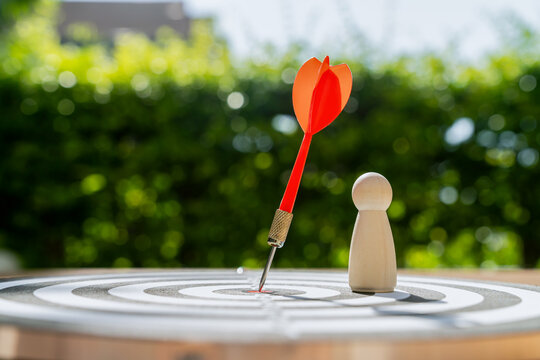 Dart in bullseye of dartboard and wooden figure standing, representing a competition to reach a goal.