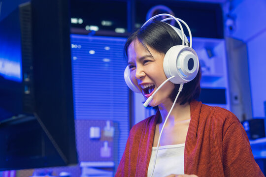 Young Asian woman playing online computer game with headset at home, esports and live streaming concept.