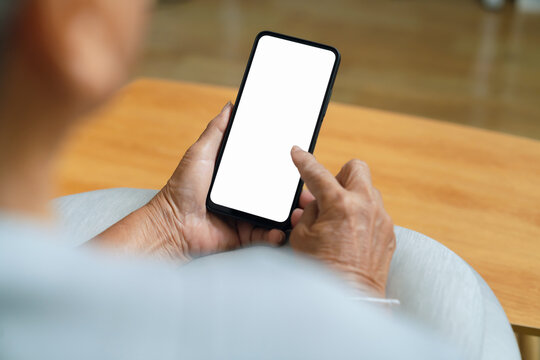 Close-up of an elderly woman hand holding a smartphone while sitting on a sofa at home.