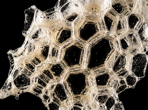 Macro close-up of golden hexagonal bubble structures forming a honeycomb pattern on a black background