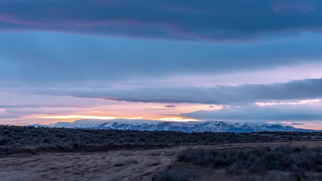View of snow-capped mountains at sunset with a dirt road and sagebrush in the foreground in Boise, Idaho, United States.