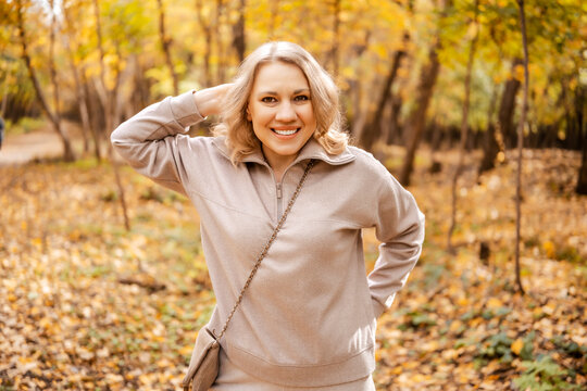Cheerful woman resting in autumn park posing with hand behind head &mdash; outdoor leisure. Digital detox concept. Relaxed person walking outside feeling vitality and connection with beautiful nature.