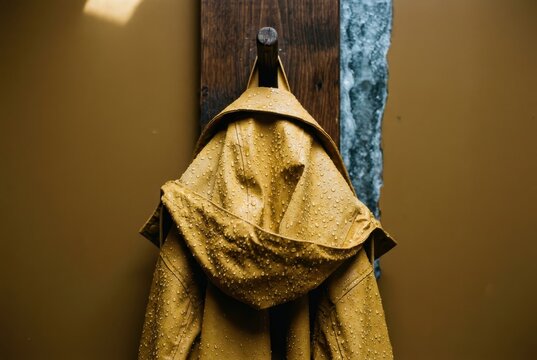 Mackintosh raincoat hanging on hook covered in raindrops and warm moody light